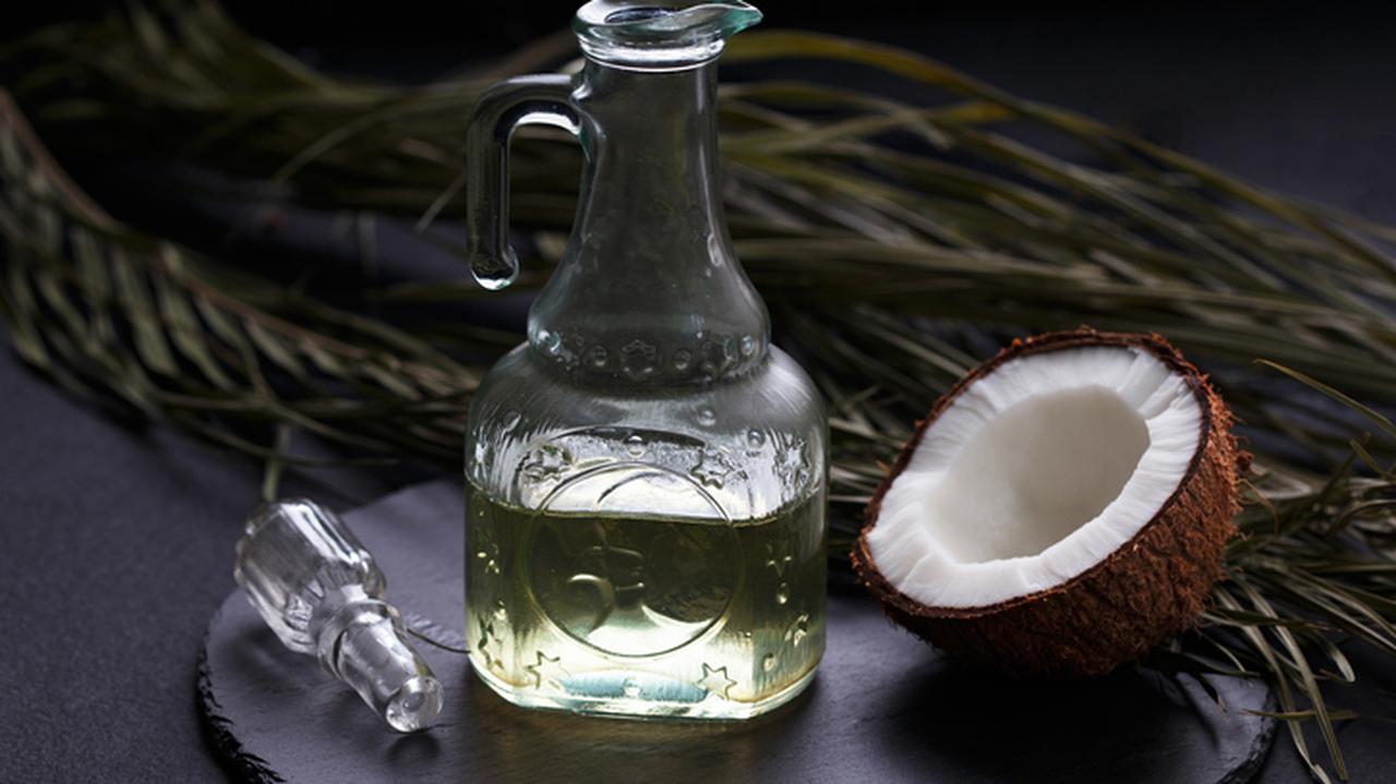 Szklany flakonik z olejem obok połówki kokosa. Olej kokosowy