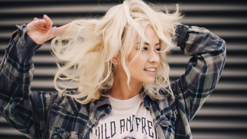 Uśmiechnięta blondynka w kraciastej koszuli. Koloryzacja włosów. Trendy. Włosy blond.