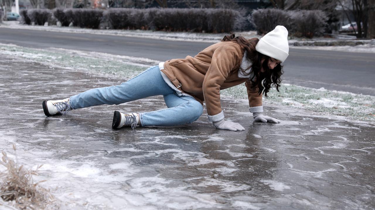 Młoda kobieta próbuje wstać po upadku na śliskim chodniku