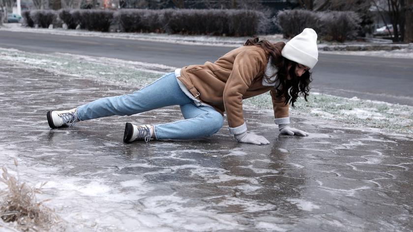 Młoda kobieta próbuje wstać po upadku na śliskim chodniku