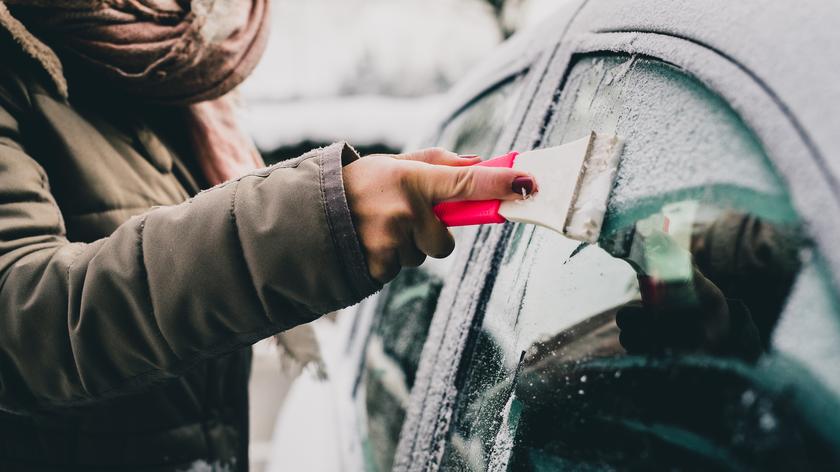 kobieta oczyszcza zamrożoną szybę w samochodzie