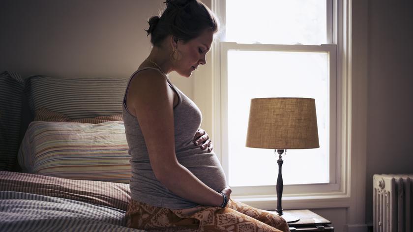 Smutna kobieta w ciąży siedzi na łóżku 