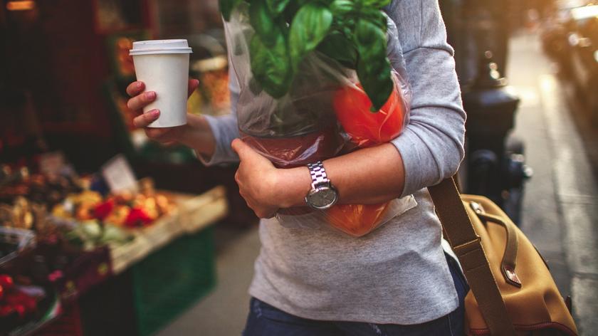kobieta w mieście niesie warzywa, trzyma kubek z kawą