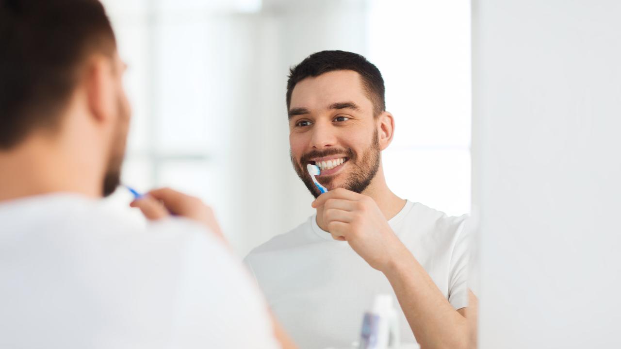 Mężczyzna, który stoi przed lustrem i myje zęby 
