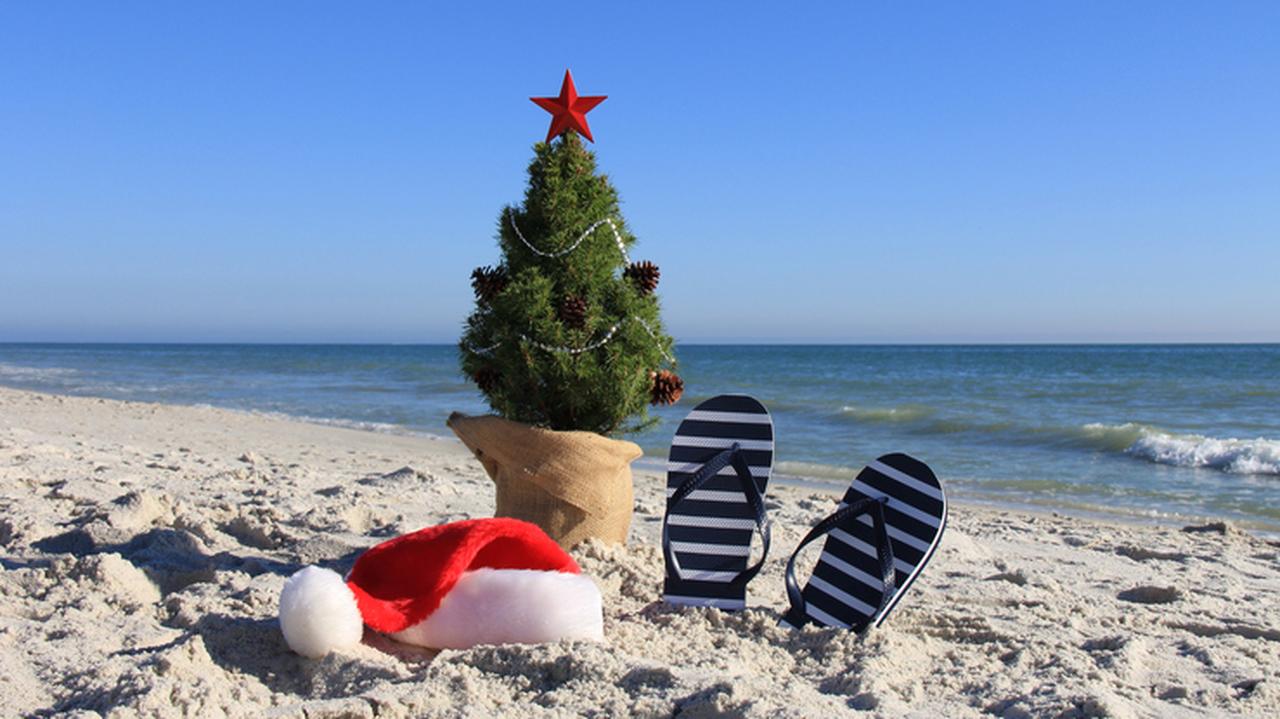 Udekorowana choinka, czapka Mikołaja i klapki na plaży. Świąteczne podróże. Święta pod palmami.
