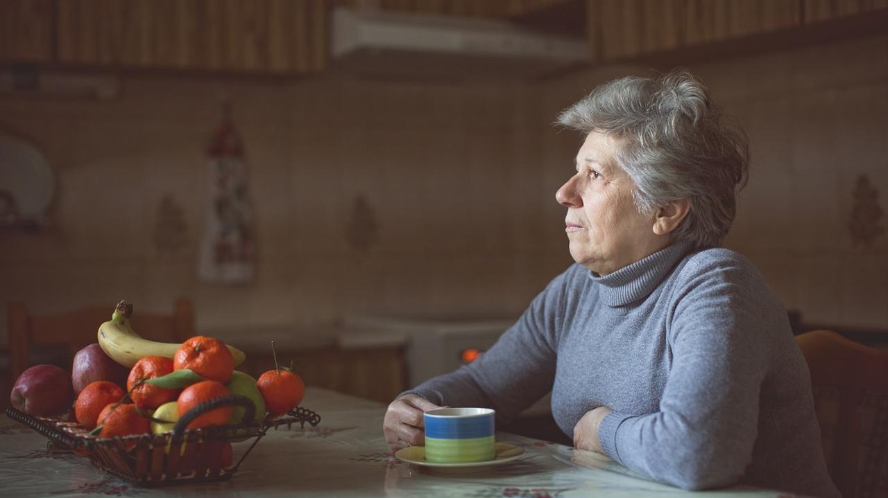 Starsza kobieta siedzi w kuchni przy stole