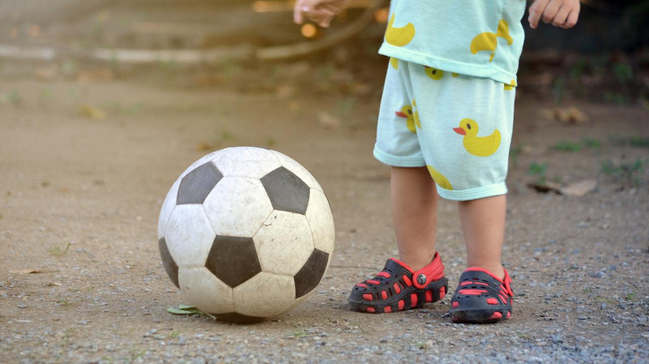 Dziecko stojące obok piłki do footbolu. 