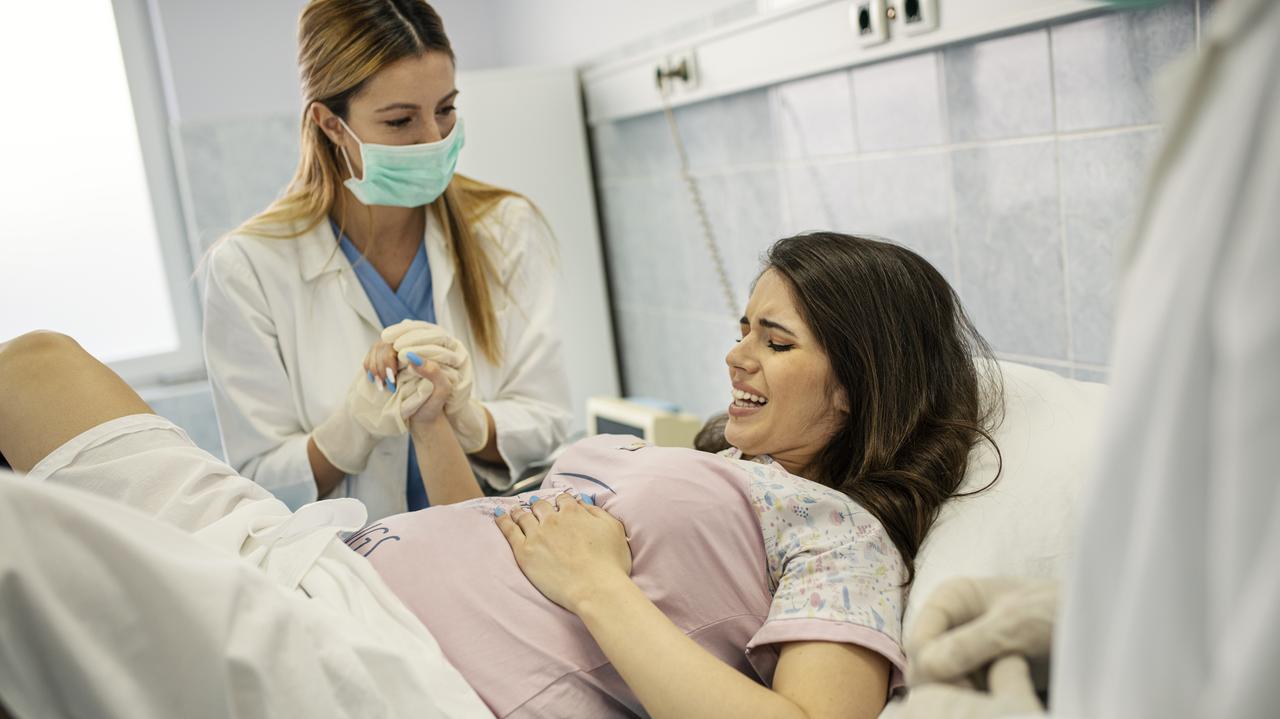 Pielęgniarka trzymająca za rękę ciężarną kobietę na sali porodowej.