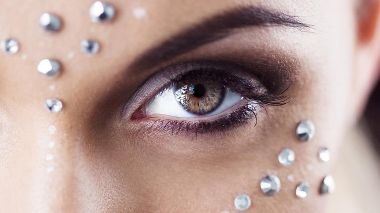 Kobiece oko podkreślone wyrazistym makijażem i elementami biżuteryjnymi. Trendy w makijażu 2022