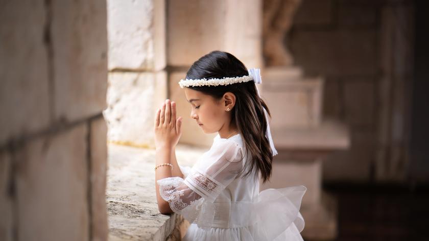 dziewczynka w sukience komunijnej klęczy i modli się 