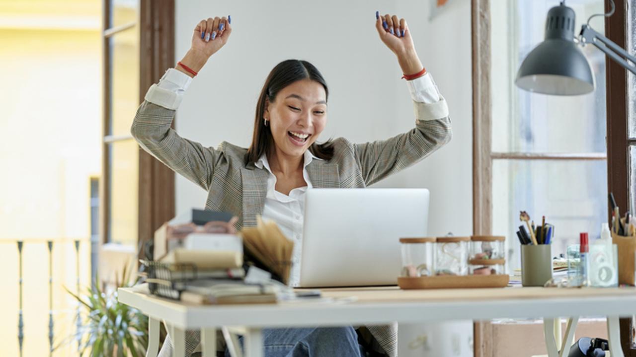 Kobieta z uniesionymi w geście triumfu rękami, pochylająca się nad ekranem komputera.