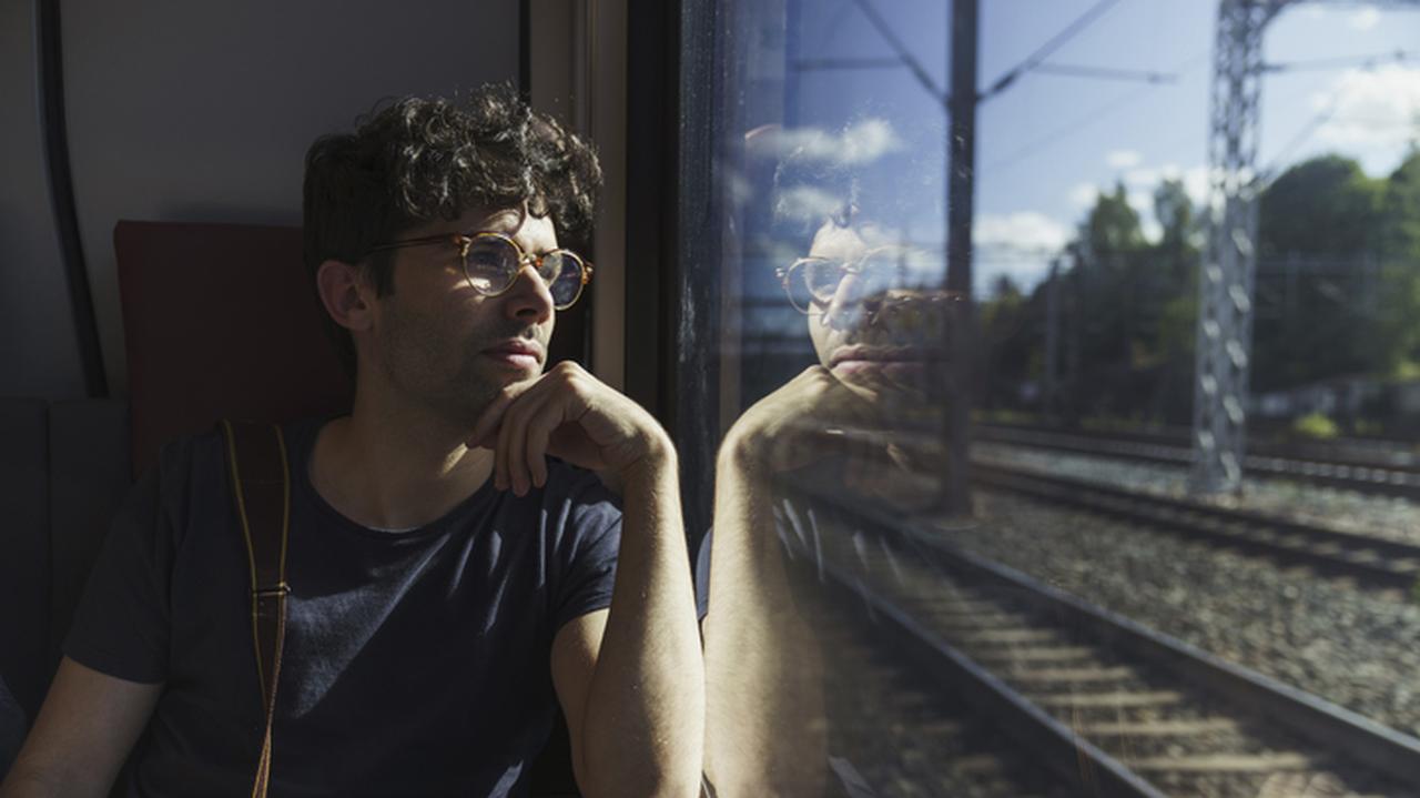 Mężczyzna wyglądający przez okno w pociągu. Podróże pociągiem. Bilety PKP