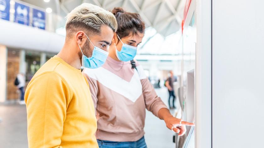 Dwie osoby w maseczkach stojące przed biletomatem