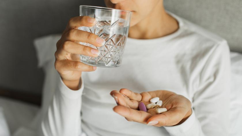 Osoba trzymająca w dłoni leki i szklankę wody