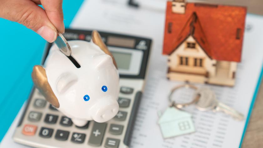 Skarbonka, kalkulator i figurka przedstawiająca dom.