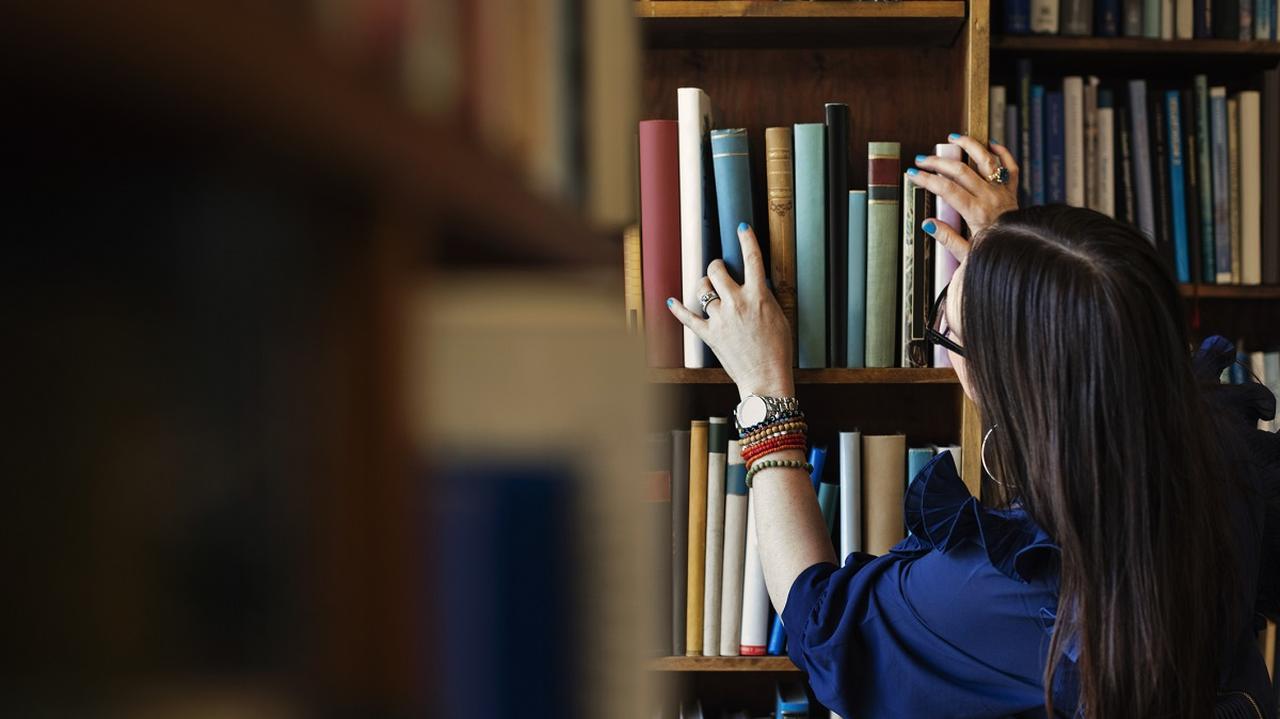 Kobieta układa książki na półkach w bibliotece