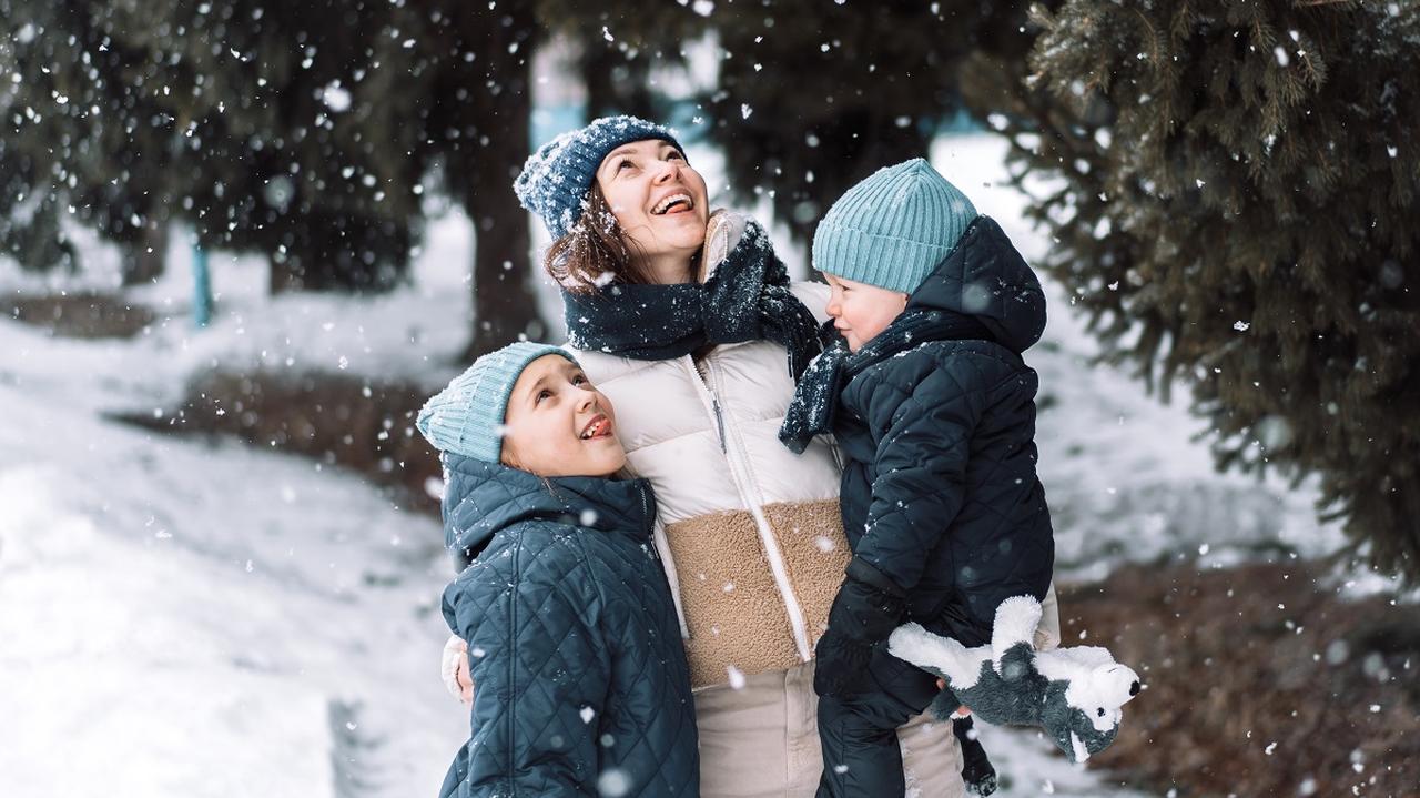 kobieta z dziećmi patrzy na padający śnieg 