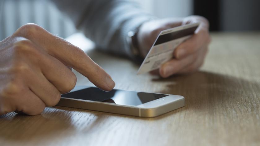 Osoba trzymająca telefon i kartę płatniczą